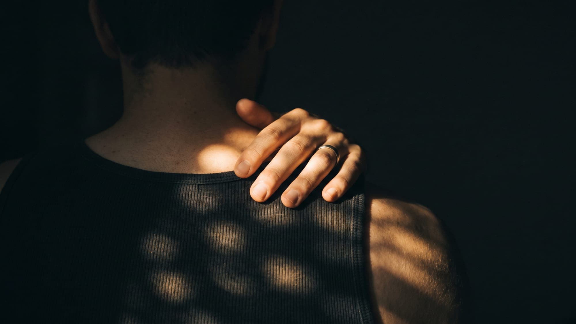 Guilt about skipping a workout: a hand resting on a shoulder, in low evening light.