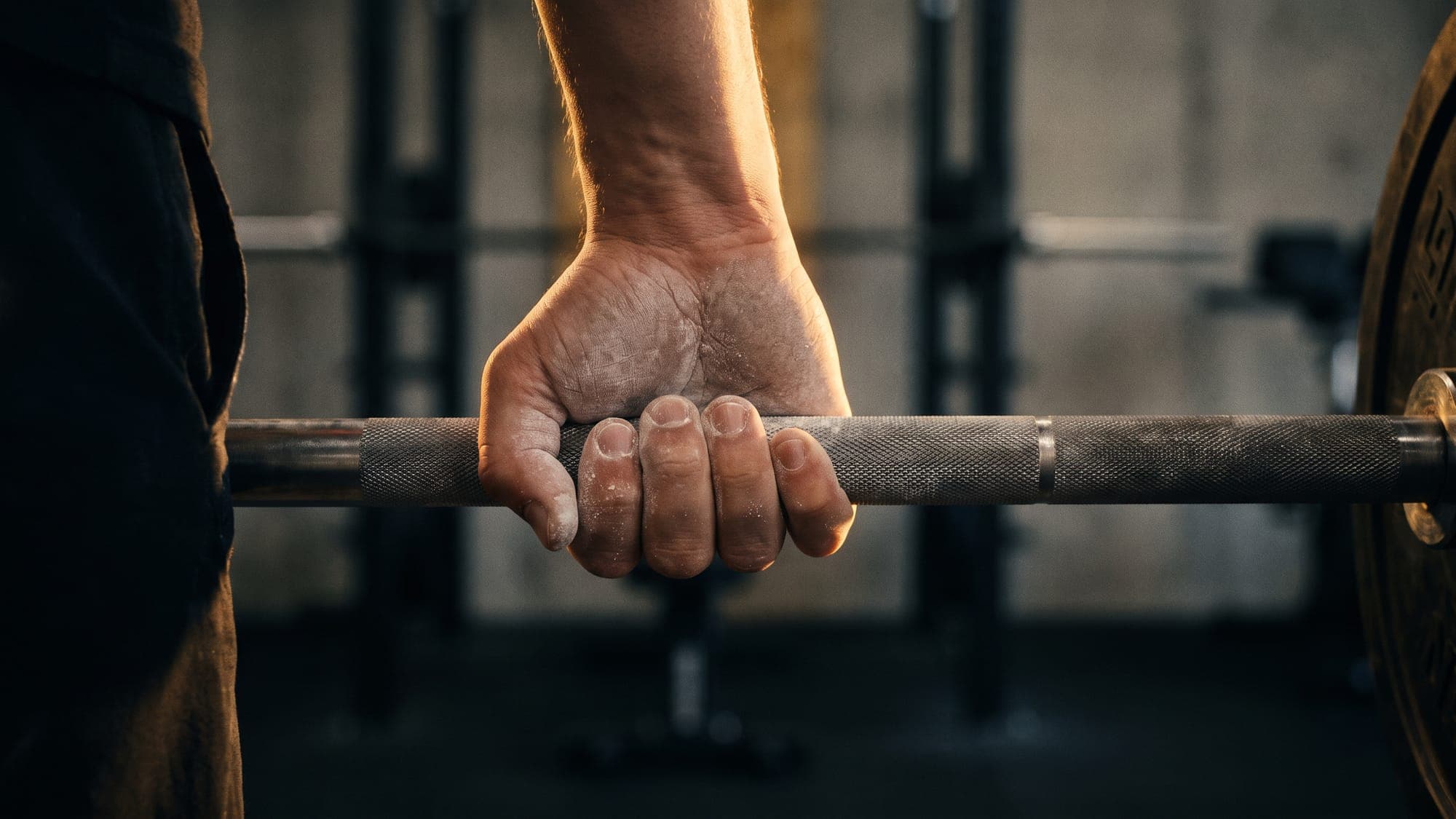 How to stay consistent with training: a chalked hand gripping a barbell.